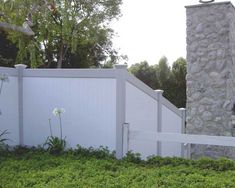 a white picket fence in front of a house with flowers growing on the grass next to it