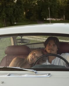 a man and woman sitting in the back seat of a white car, looking at each other