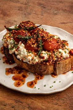 a white plate topped with a piece of bread covered in toppings on top of a wooden table