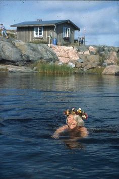 a woman floating in the water with a flower crown on her head and some rocks behind her