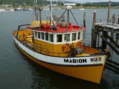 a yellow and white boat is docked at the dock with other boats in the water