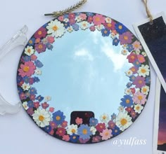 there is a mirror with flowers on it next to some pictures and a cell phone