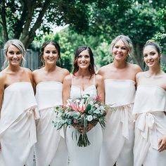 a group of women standing next to each other wearing white dresses and holding bouquets