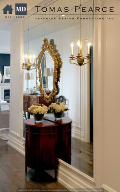 a mirror and some flowers on a table in front of a doorway with a bed