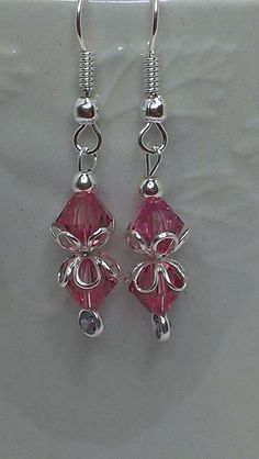 pair of earrings with pink crystal beads and silver wire on white background, close up