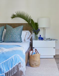 a bed with blue and white pillows on top of it next to a basket filled with flowers