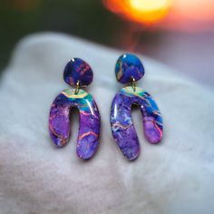 two purple and blue earrings sitting on top of a white cloth