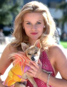 a woman is holding a small dog in her arms and posing for the camera while wearing a dress