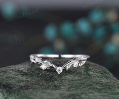 a white gold wedding band with leaves on the side, sitting on top of a rock