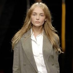 a woman with long blonde hair walking down a runway wearing a gray blazer and white shirt