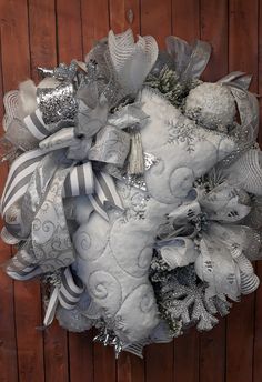 a wreath with silver and white decorations hanging on a wooden wall