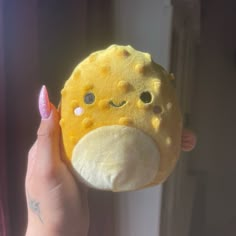 a hand holding a yellow stuffed animal with eyes and nose on it's face