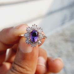 a person holding a ring with a purple stone in it