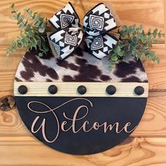 a welcome sign hanging on the side of a wooden wall with two bows and greenery