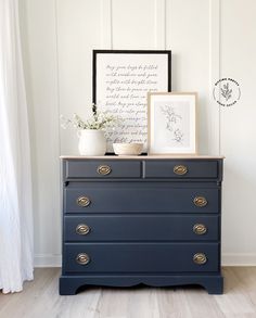 a blue dresser with two pictures on top of it and a plant in the corner