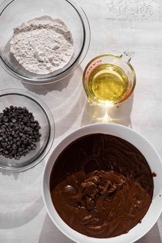 three bowls filled with different types of food on top of a white tablecloth next to an empty glass bowl