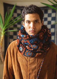 a young man wearing a scarf in front of a potted plant and tiled wall