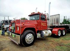 a red semi truck parked on top of a grass covered field