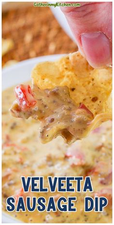 a hand holding a tortilla chip over a bowl of velveeta sausage dip