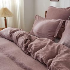 an unmade bed with pink linens and pillows