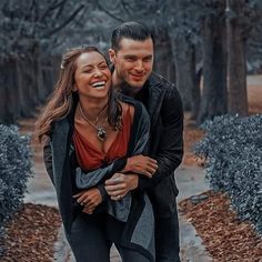 a man and woman walking down a path in the woods with their arms around each other