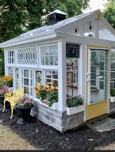 a small white greenhouse with lots of flowers in the front and windows on each side