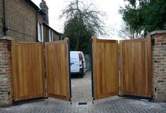 an open wooden gate on the side of a brick road next to a white van