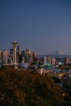 the seattle skyline is lit up at night with snow capped mountains in the back ground