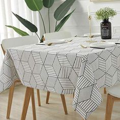 a dining room table covered with a black and white geometric design, next to a potted plant