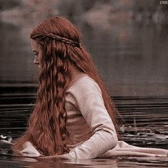 a woman with long red hair sitting in the water