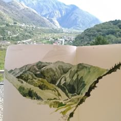 an open book with watercolors on it and mountains in the backgroud