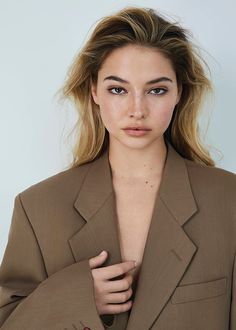 a woman in a brown suit with her hands on her chest, looking at the camera