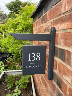 a house number sign mounted to the side of a brick wall next to a garden