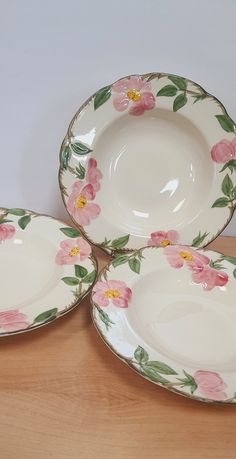 three plates with pink flowers on them sitting on a wooden table top next to each other