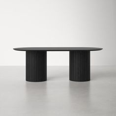 an oval table with two black columns on the top and bottom, in front of a white wall