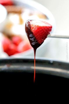 a spoon full of chocolate covered strawberries being dipped with melted sugar and syrup from a pot