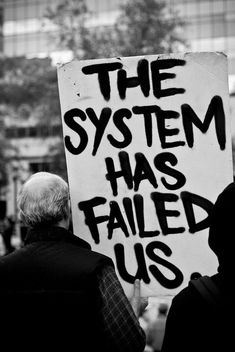 black and white photograph of protestors holding sign that says the system has failed us