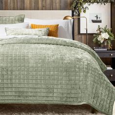 a bed with green bedspread and pillows on top of it next to a night stand