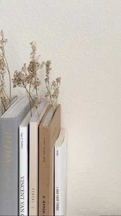 two books are sitting next to each other on a shelf with dried flowers in it