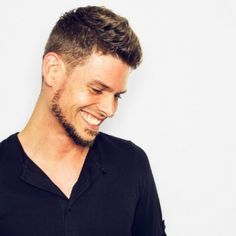 a man smiling and looking down at his cell phone while wearing a black polo shirt