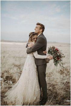 a bride and groom embracing in the middle of an open field with tall dry grass