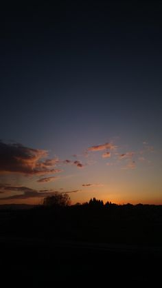 the sun is setting behind some trees and hills