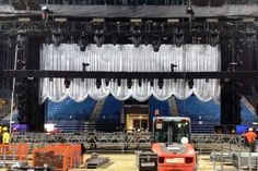 the stage is set up for an event with white drapes on it and workers in orange vests