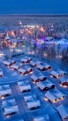 an aerial view of snow covered houses and trees in the background at night with lights on