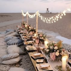 a long table is set up on the beach with candles and place settings for dinner