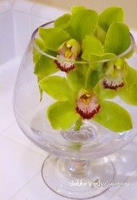 a glass vase filled with green flowers on top of a white countertop next to a mirror