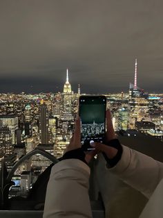 a person holding up a cell phone in front of a cityscape at night