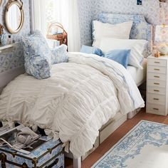 a bedroom with blue and white wallpaper, bed linens, and a mirror