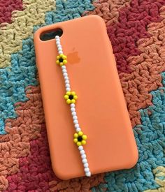 an orange iphone case with a beaded necklace on it sitting on a colorful blanket