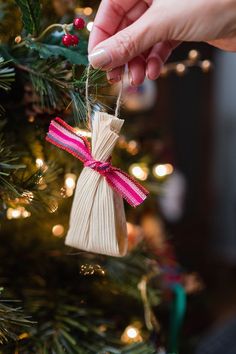 a hand holding a string ornament on top of a christmas tree